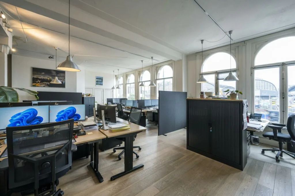 Modern kantoorgebouw aan de De Ruijterkade met werkplekken, grote ramen en uitzicht op station Amsterdam Centraal.